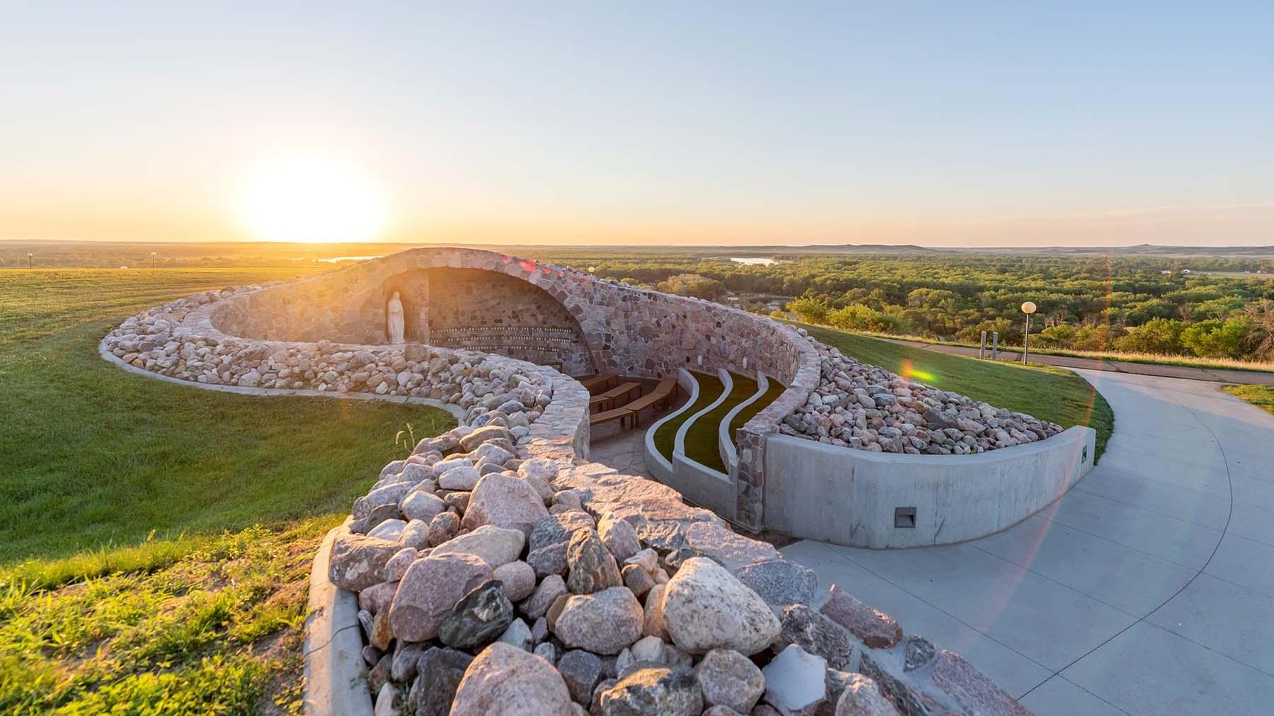 A view of the Grotto with the sun setting over the horizon and a view of Bismarck North Dakota and the Missouri River in the background.